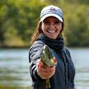 Giulia Bianchi sorridente, tiene un grande black bass appena pescato, con la sua canna Acquamarina in bella mostra sullo sfondo di un lago tranquillo.