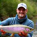 Marco Rossi contento con la sua cattura, in piedi accanto a un fiume, con la sua canna Acquamarina ben visibile.