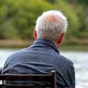 Simone Verdi, un uomo anziano e saggio, siede comodamente sulla riva di un fiume con la sua canna feeder personalizzata Acquamarina, godendosi la giornata.